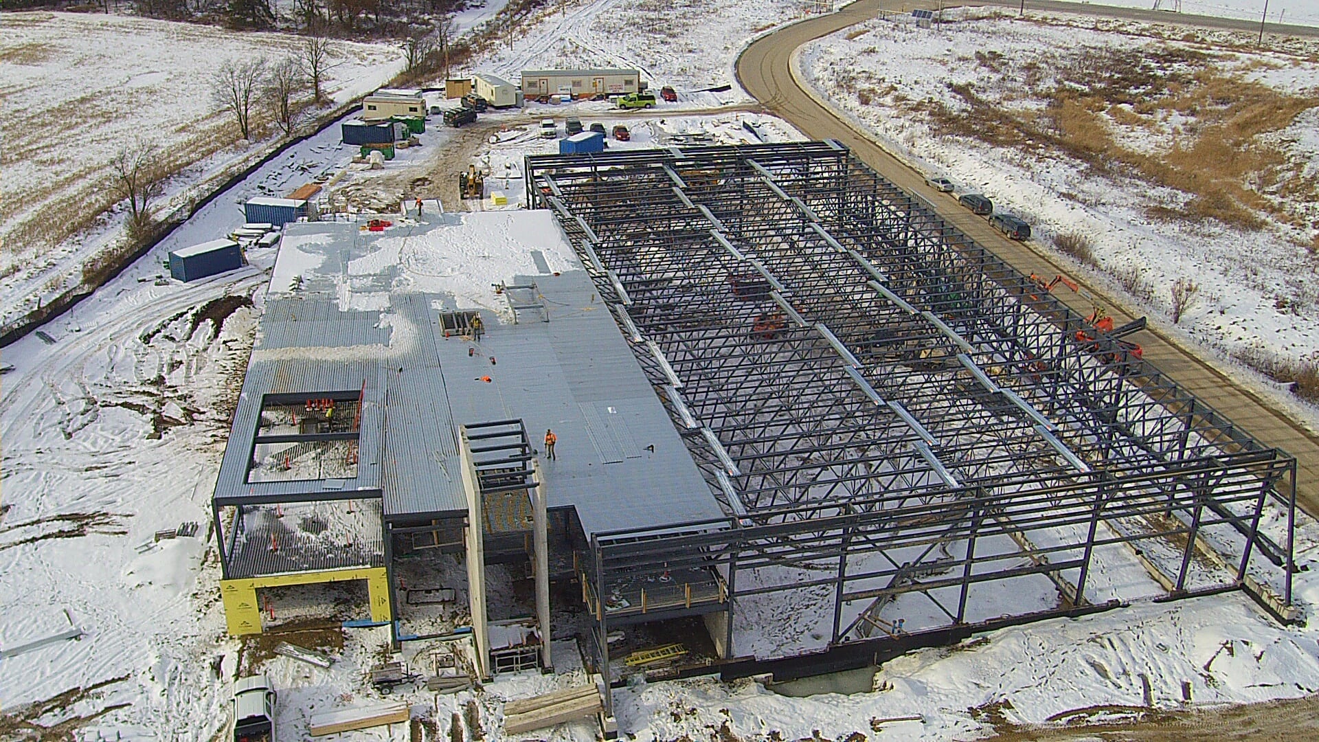 An aerial view of the station under construction in snow: the decked office block at the left and the open steel frame of the apparatus bays at the right.